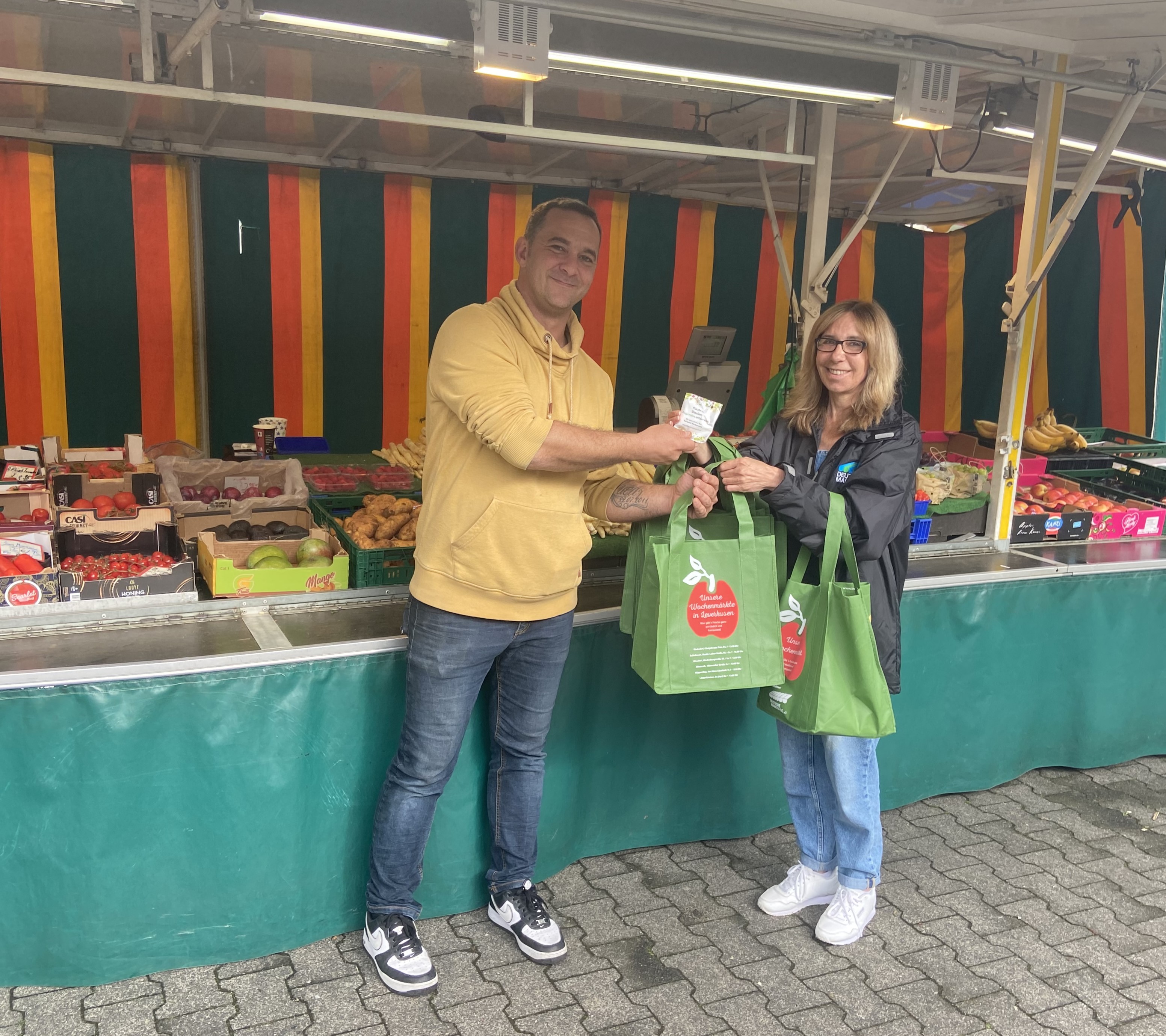 Obst- und Gemüsehändler René Möller freut sich über die Markttasche und den Knabbersnack, von Heidi überreicht. // Foto: Deutsche Marktgilde